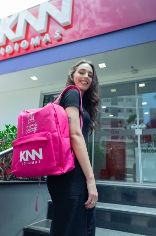 Menina na entrada de uma unidade da KNN com um mochila rosa nas costas.