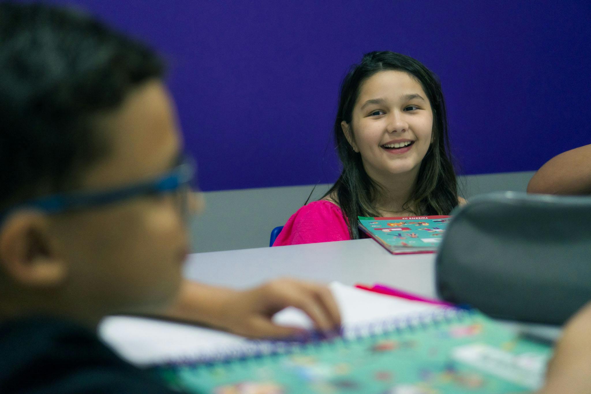 Criança em uma sala de aula sorrindo e com expressão de felicidade/alegria.