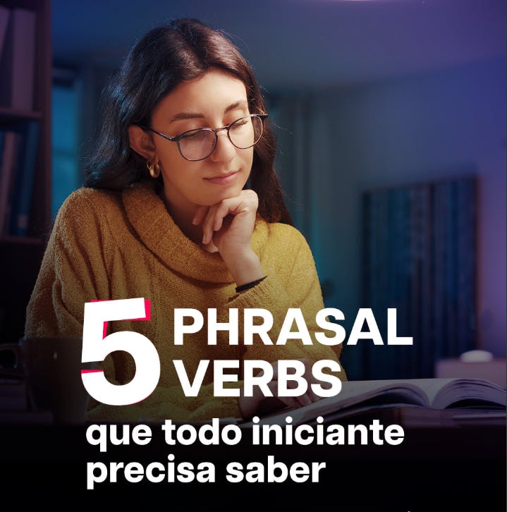 Uma mulher de óculos, com a mão no queixo e olhando para um livro que está em cima da mesa. A imagem possui o lettering: "5 Pharsal Verbs que todo iniciante precisa saber".
