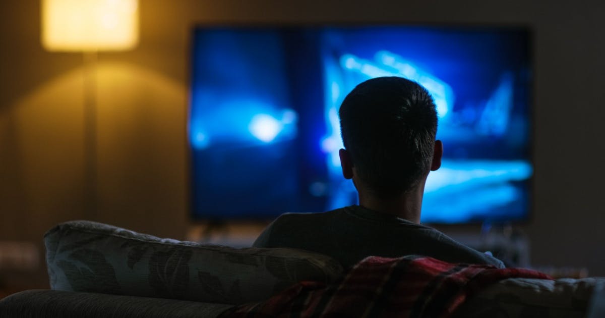 Uma homem de costas, sentada no sofá e assistindo filmes.