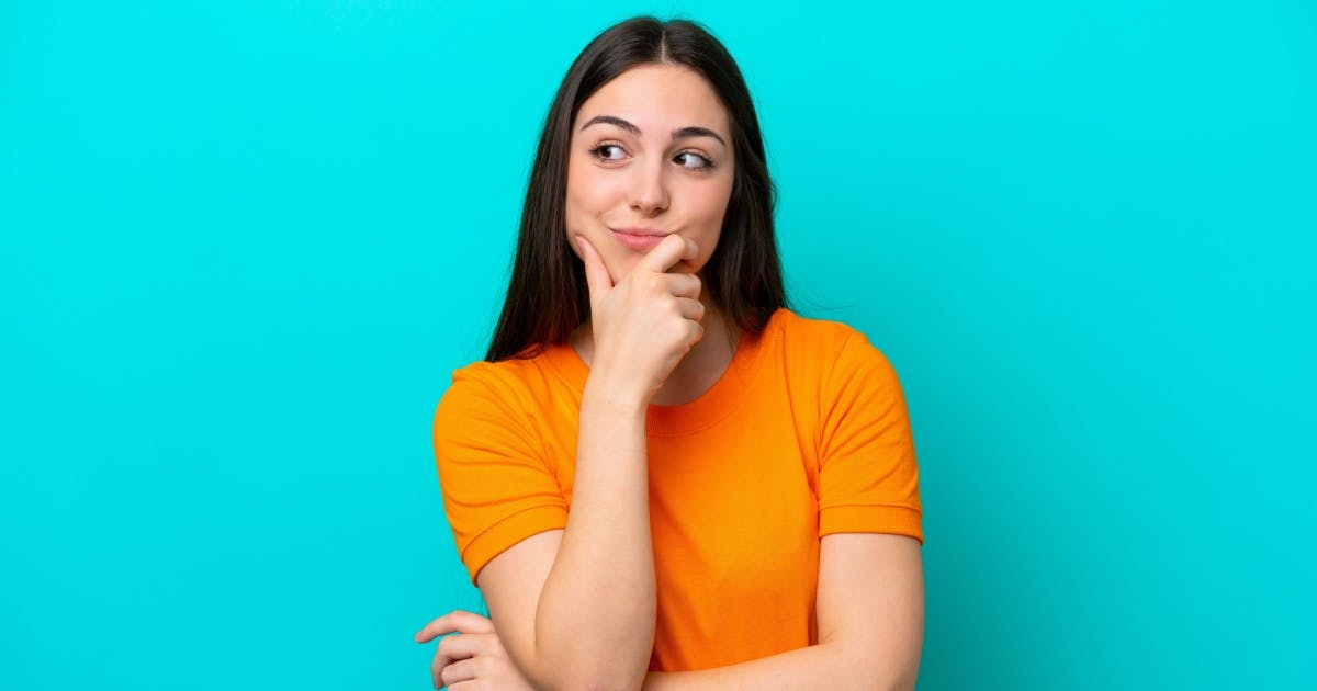Mulher jovem com a mão direita no rosto e com expressão de dúvida.