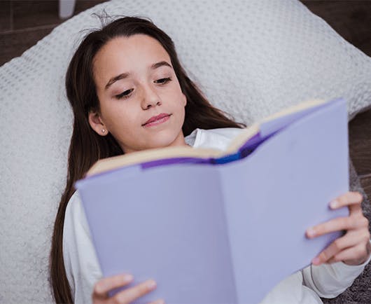Criança deitada na cama lendo um livro.