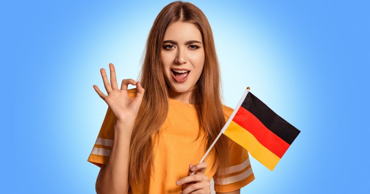 Mulher ruiva fazendo sinal com as mãos e com a bandeira da Alemanha na mão.