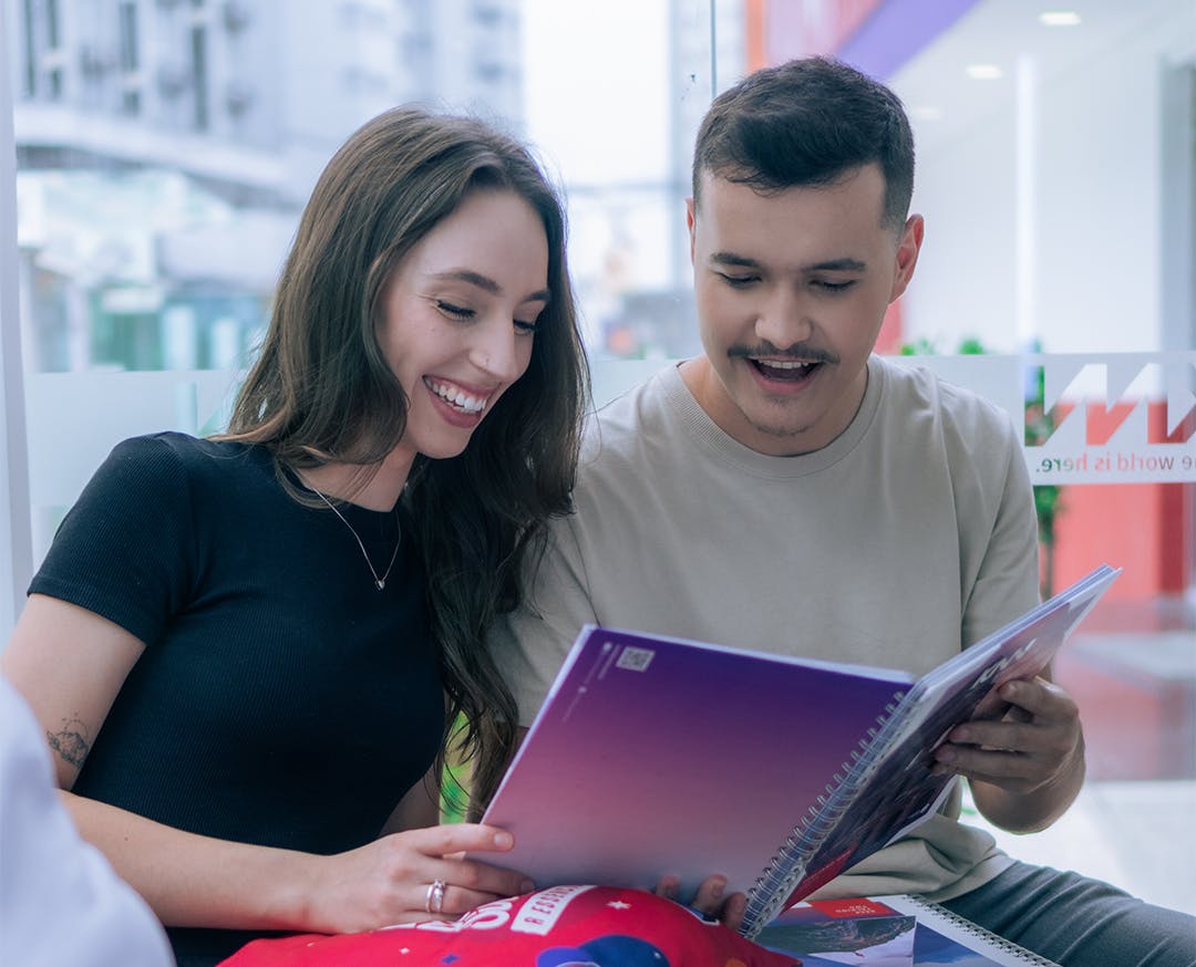 Alunos olhando para o livro da KNN Idiomas sorrindo e felizes.