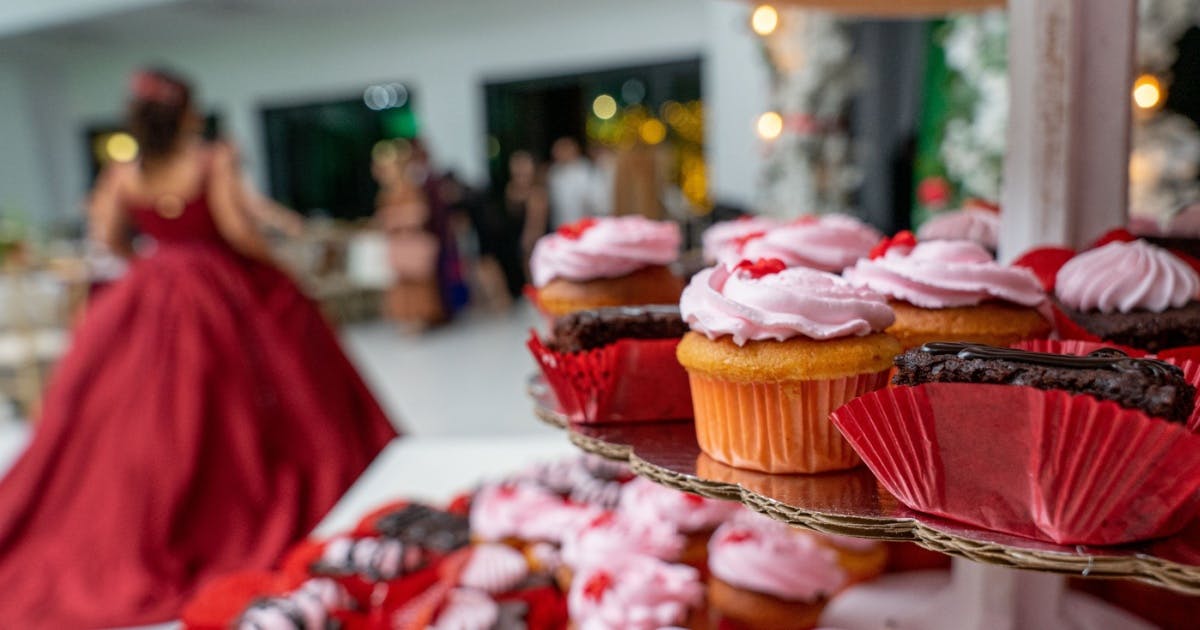 Foto de doces e, ao fundo, com desfoque na foto, uma menina com vestido de festa de 15, tradicional em países latino-americanos.