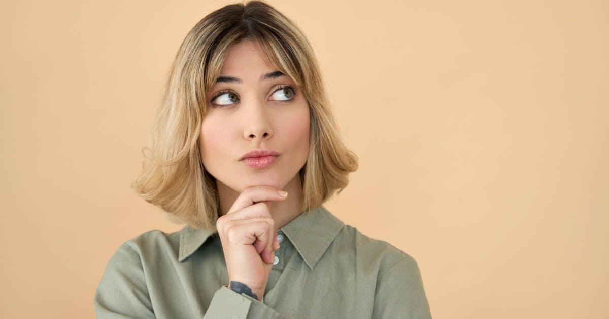 Mulher com a mão direita no queixo e com expressão de dúvida.