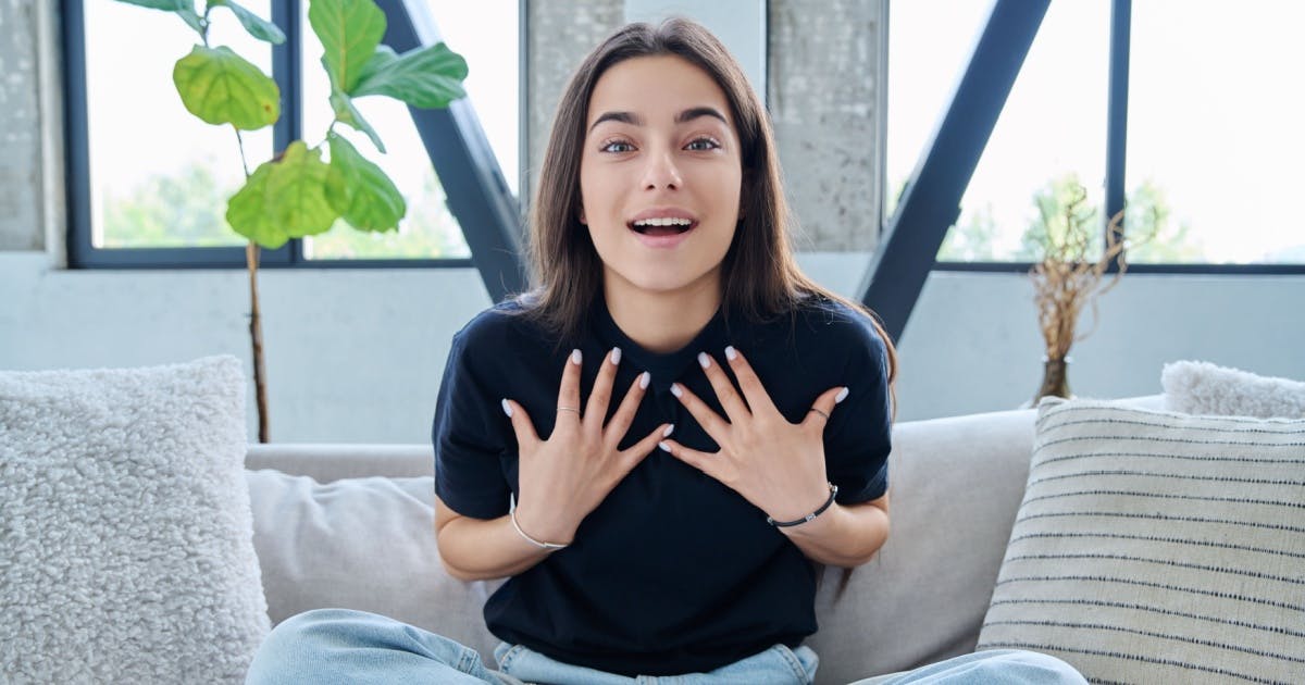 Mulher olhando para a foto e com expressão de surpresa, com as duas mãos na região do peito.