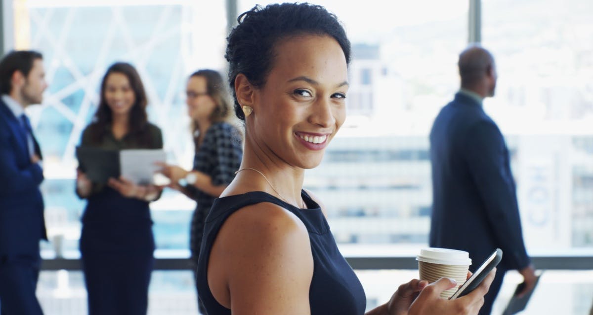 Mulher olhando para a foto sorrindo e com um café na mão.