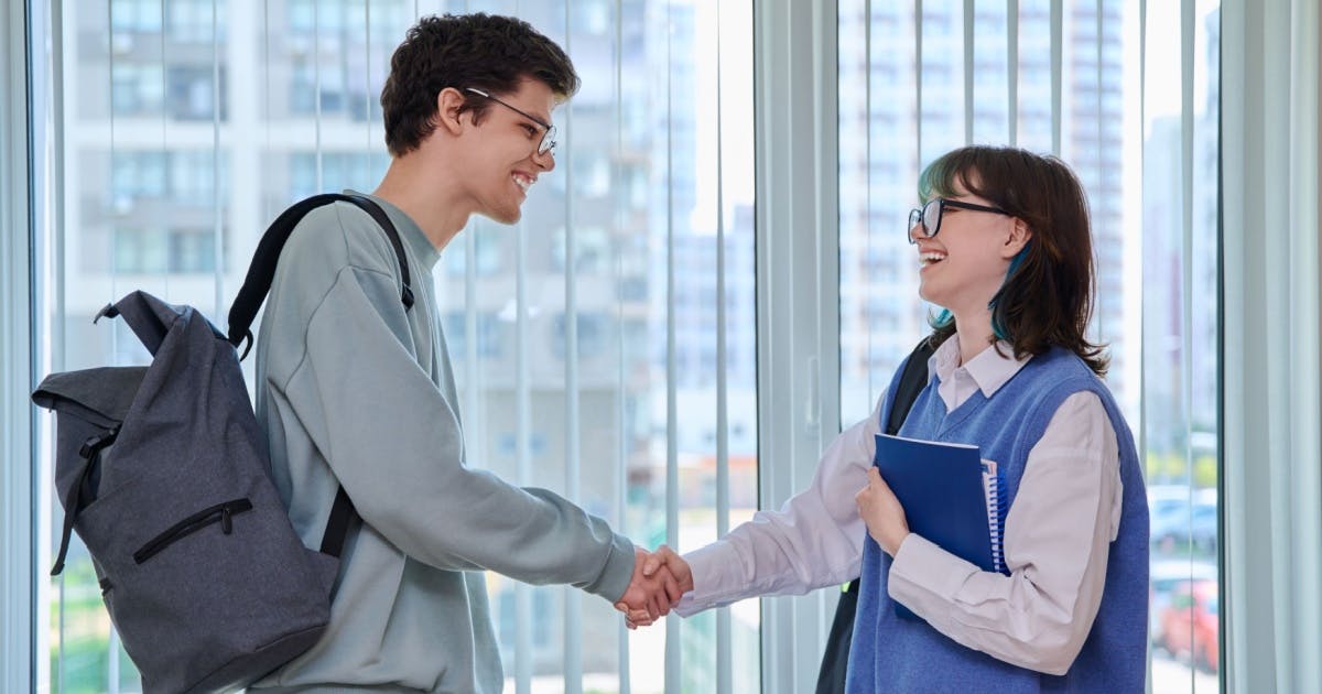 Homem e mulher jovens se cumprimentando e sorrindo. Eles estão com mochilas nas costas.