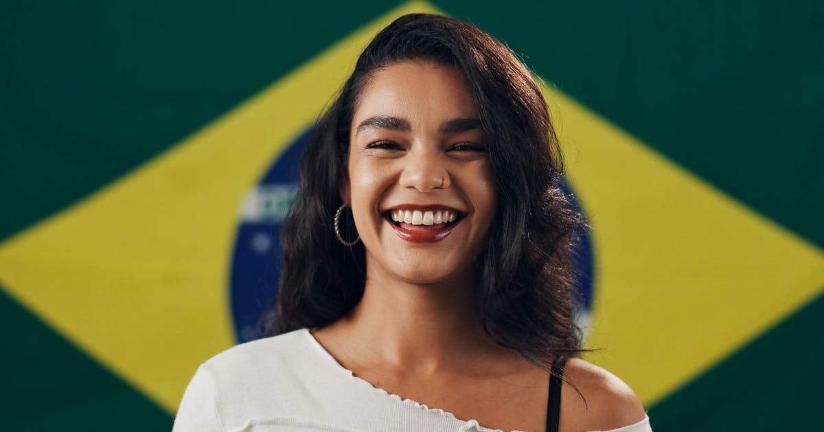 Mulher sorrindo e com expressão de felicidade e, ao fundo, uma bandeira do Brasil.
