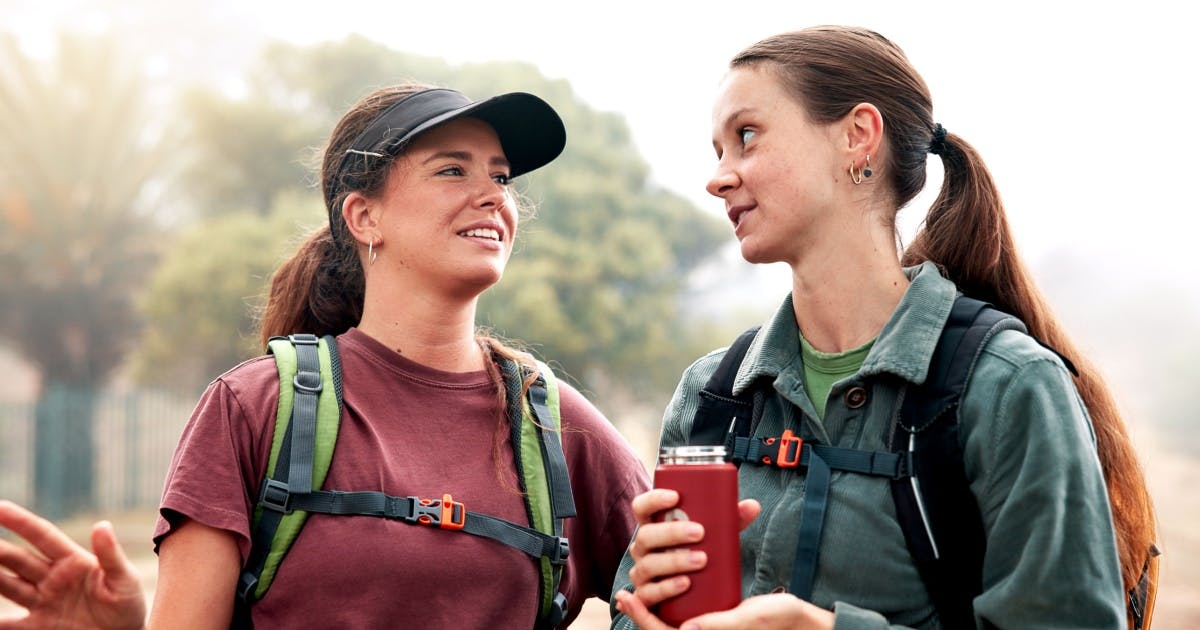Duas mulheres conversando e se olhando. Uma está com uma garrafa de água e a outra de boné.