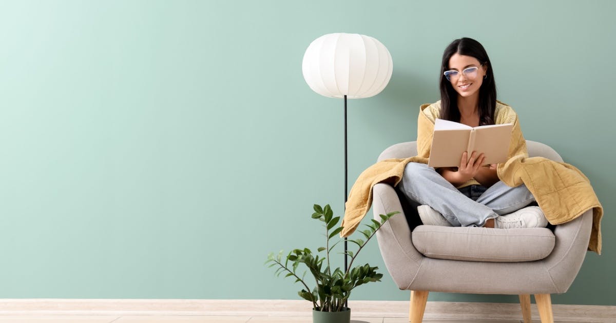Mulher sentada em uma poltrona lendo e com expressão de felicidade. 