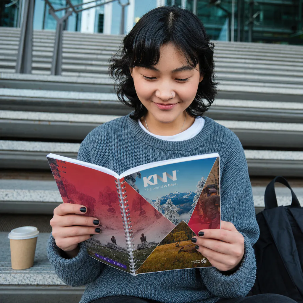 menina com copo de café ao lado, com livro da KNN aberto