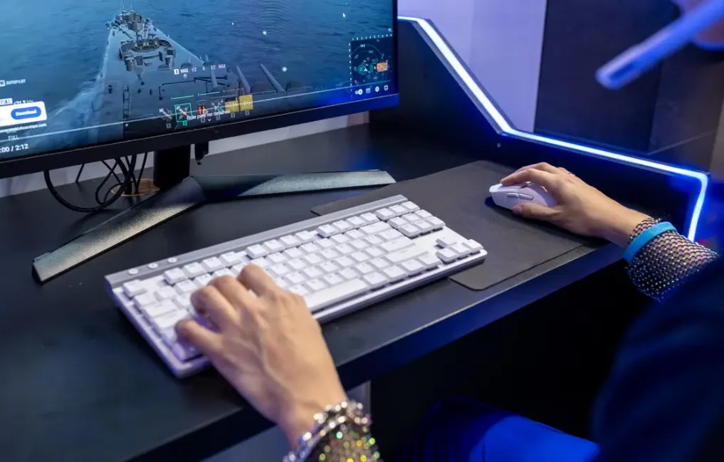 Pessoa usando teclado e mouse em estação de trabalho com múltiplos monitores, incluindo imagem de navegação marítima e interfaces de controle, em ambiente tecnológico e iluminado por LEDs azuis