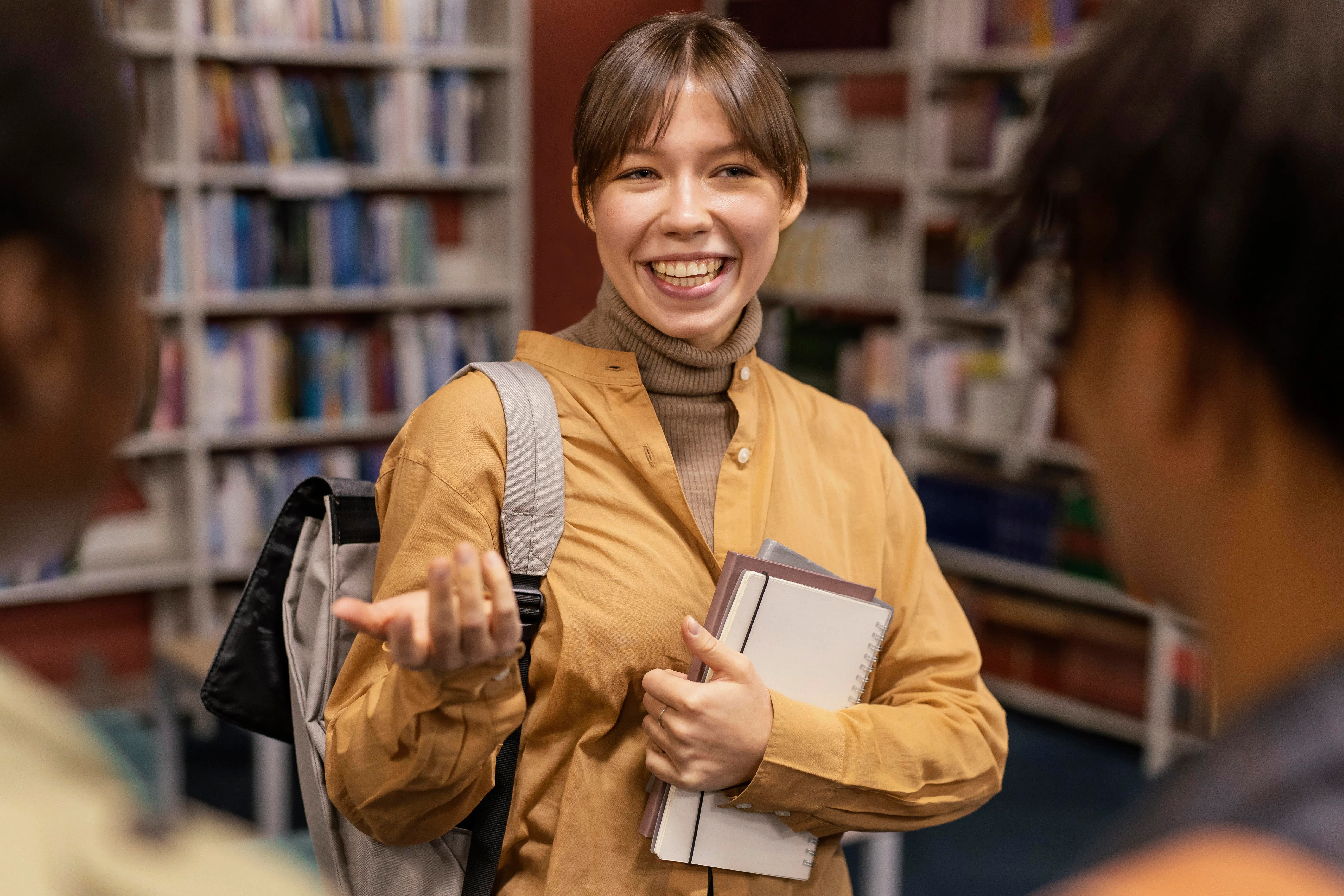 jovem com livro na mão, conversando com amigos em uma biblioteca