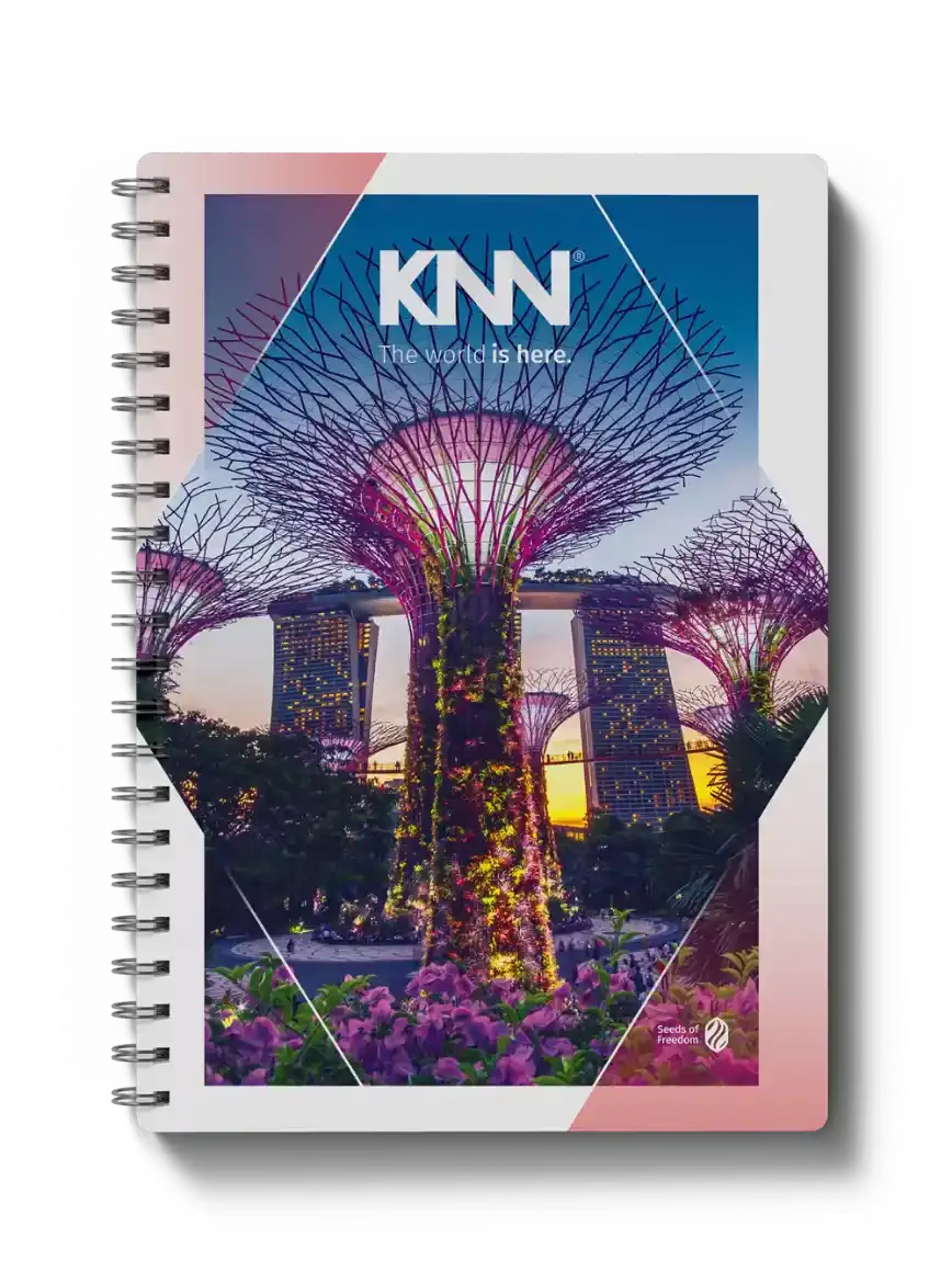 Capa de caderno com a marca KNN The world is here, mostrando a árvore metálica do Gardens by the Bay com luzes coloridas e arranjos floridos, além do selo Seeds of Freedom.