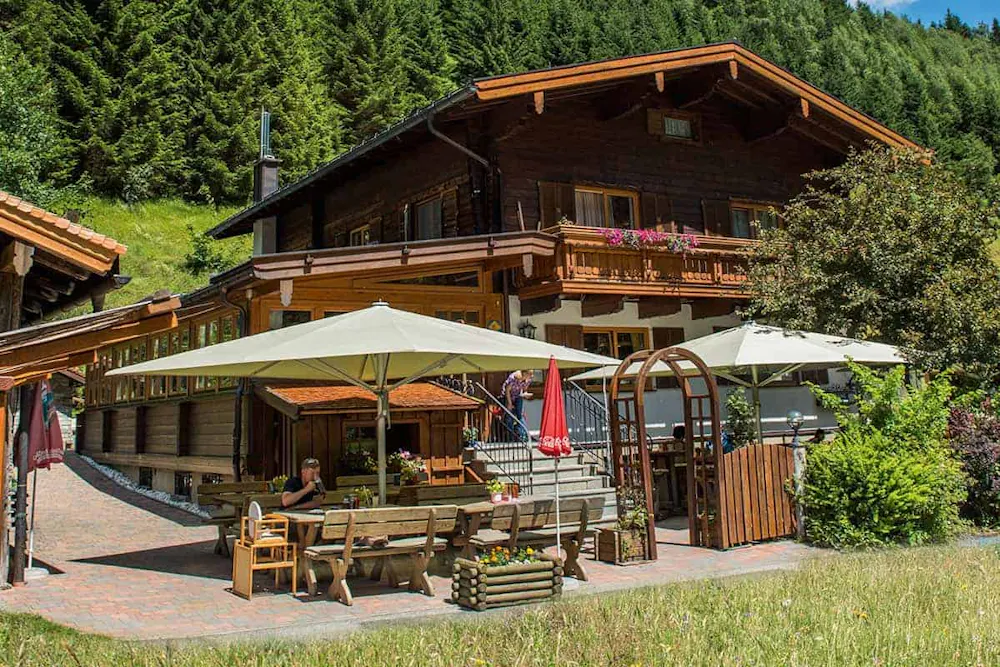 Landgasthaus Weixen in Rauris. Man sieht ein schönes, traditionalles, österreichische Haus am Bild mit Terasse. Finde deine Ferienwohnung bei we rent apartments