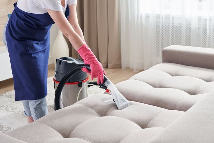 Woman vacuum cleaning suede sofa