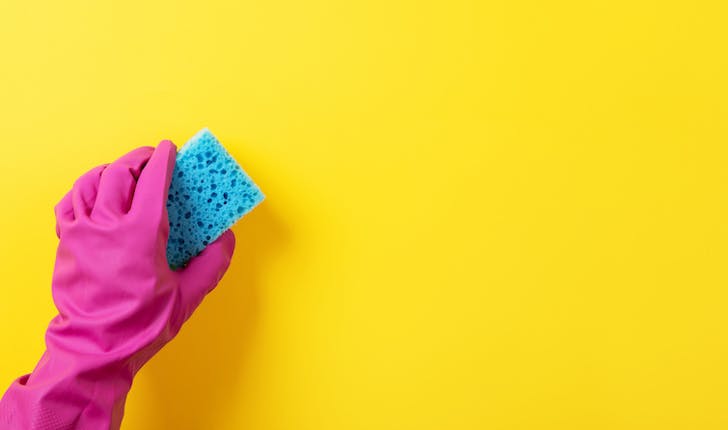 pink rubber glove holding blue sponge on yellow background