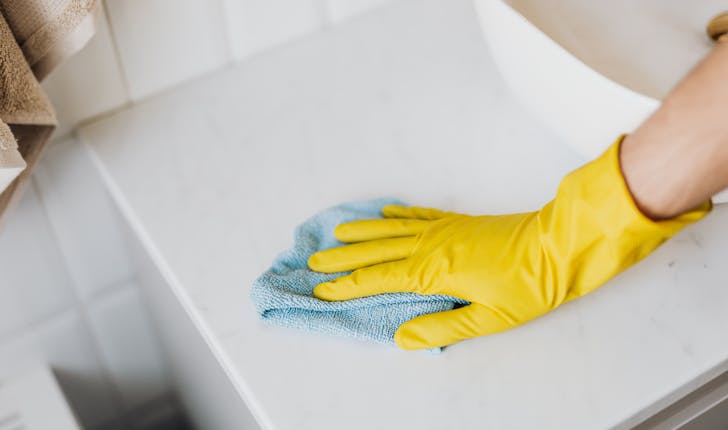cleaner drying the sink wearing yellow gloves
