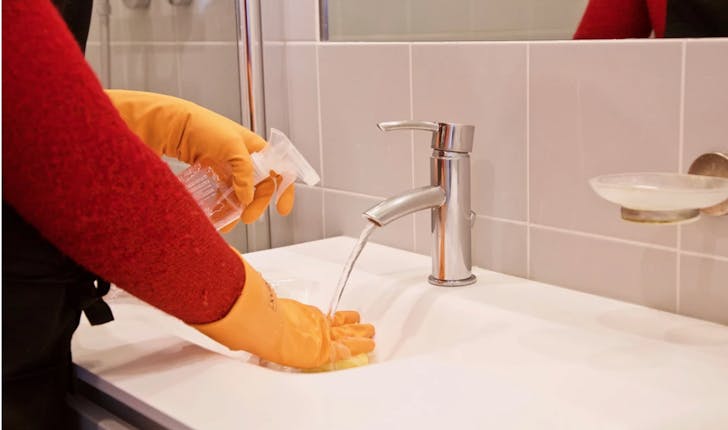 cleaning lady cleaning the sink wearing yellow gloves 