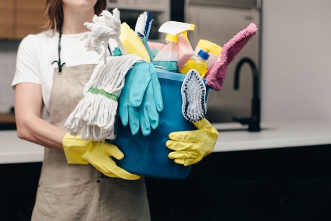 Une aide ménagère à domicile tient un sceau rempli d'outils et de produits de nettoyage après travaux.