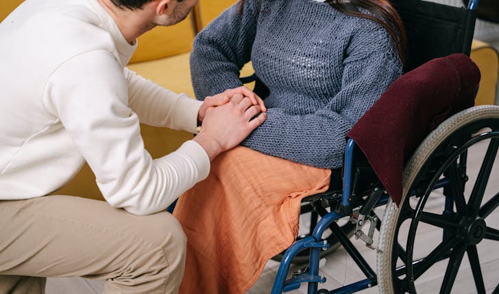Homme à genoux qui tient les mains d'une femme en fauteuil roulant 