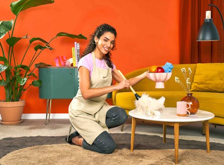 Une femme de ménage qui nettoie une table de salon avec un plumeau.