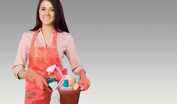 Aide ménagère souriante et tenant un saut contenant des produits de nettoyage.