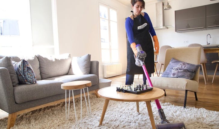 Femme de ménage passant l'aspirateur sur un tapis dans un Airbnb