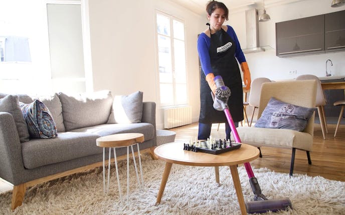 Femme de ménage passant l'aspirateur sur un tapis dans un Airbnb