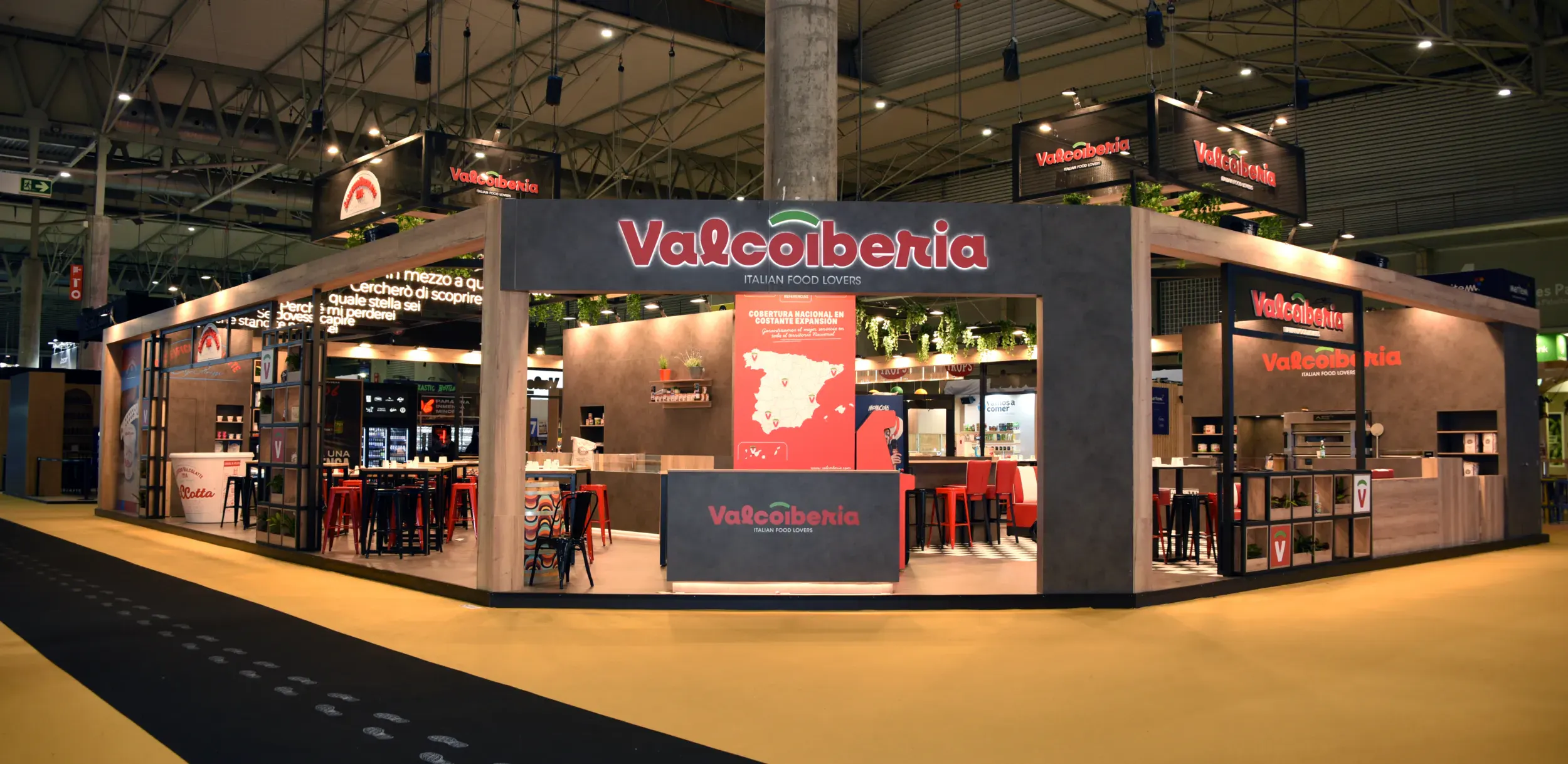 Valcoiberia Italian food corner store with red branding, wood finishes, seating area, and product displays