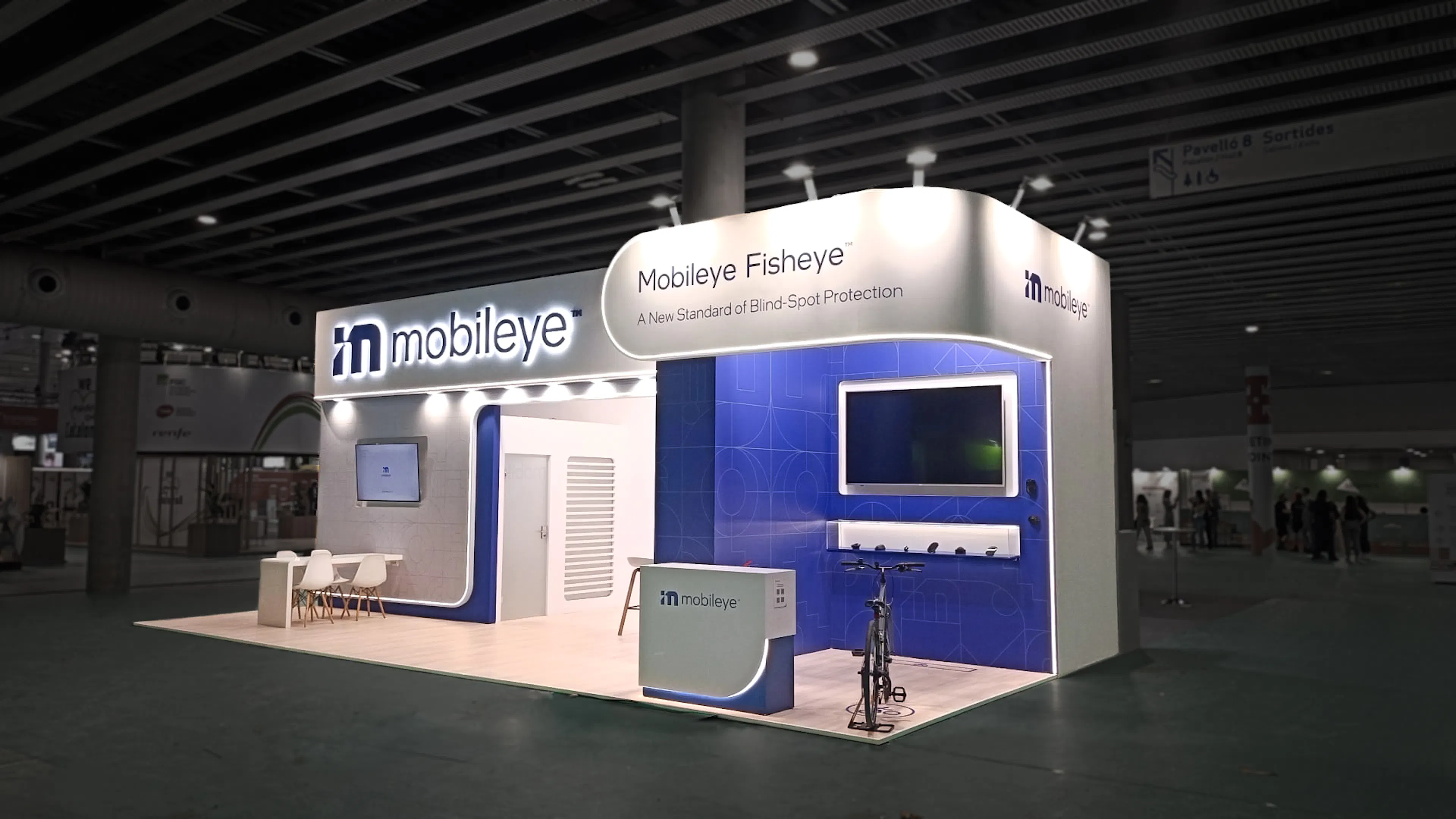 Mobileye exhibition stand with white and blue branding, "Fisheye" blind-spot technology display, seating area, and bicycle demo setup