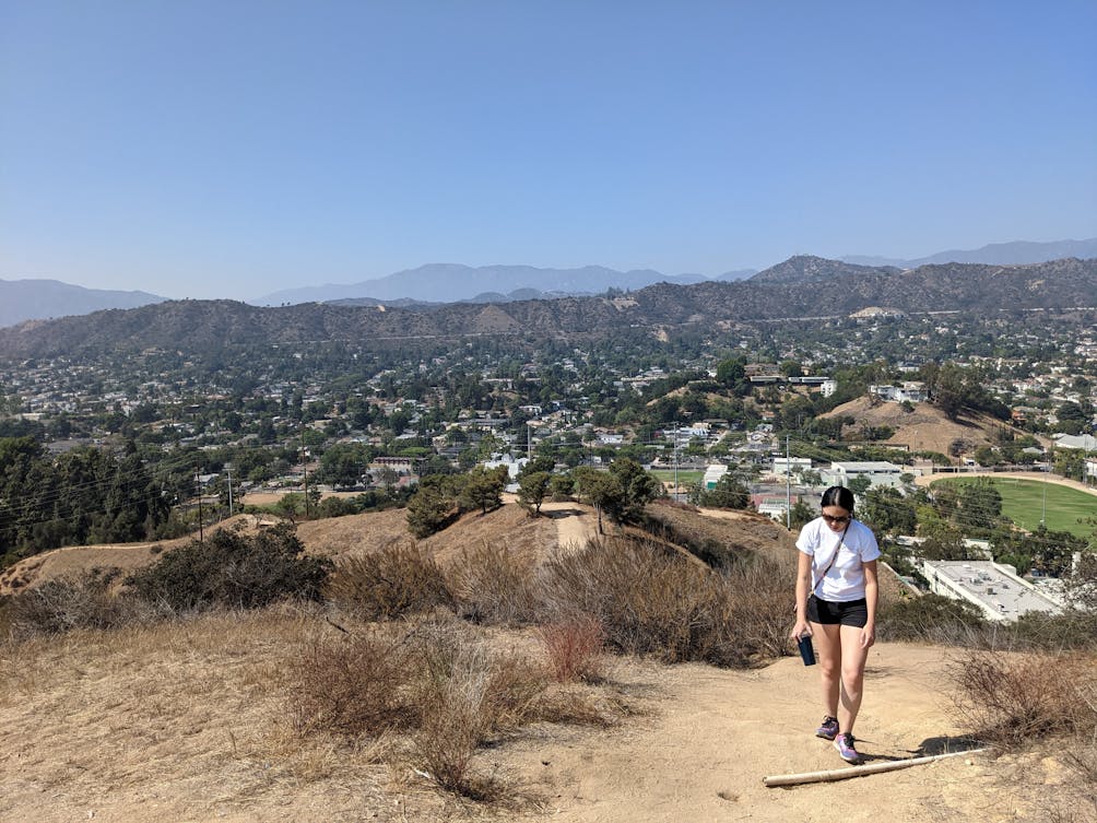 Hiker heading up a trail at Fiji Hill in Los Angeles with mountains in the background 