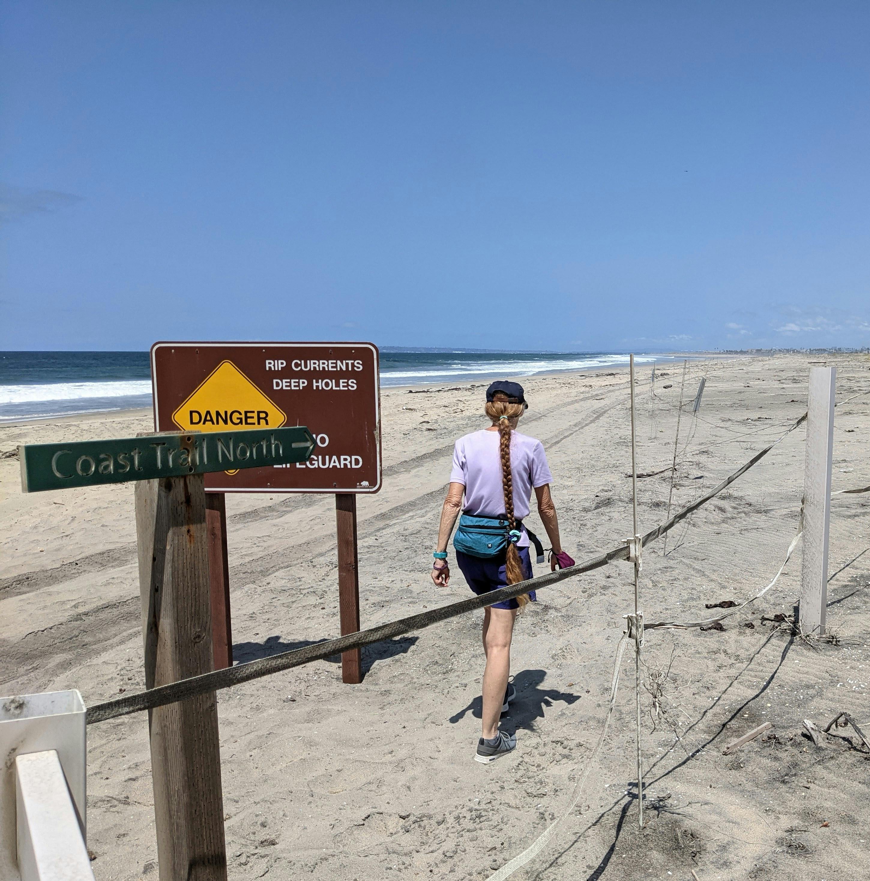 Woman hiking past a sign and onto the beach at Border Field State Park in San Diego County 