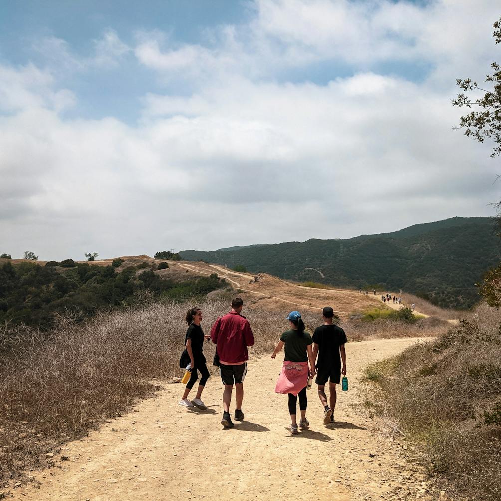 Group of four hikers on a wide dirt trail at Upper and Lower Canyonback Trails in Santa Monica Mountains 