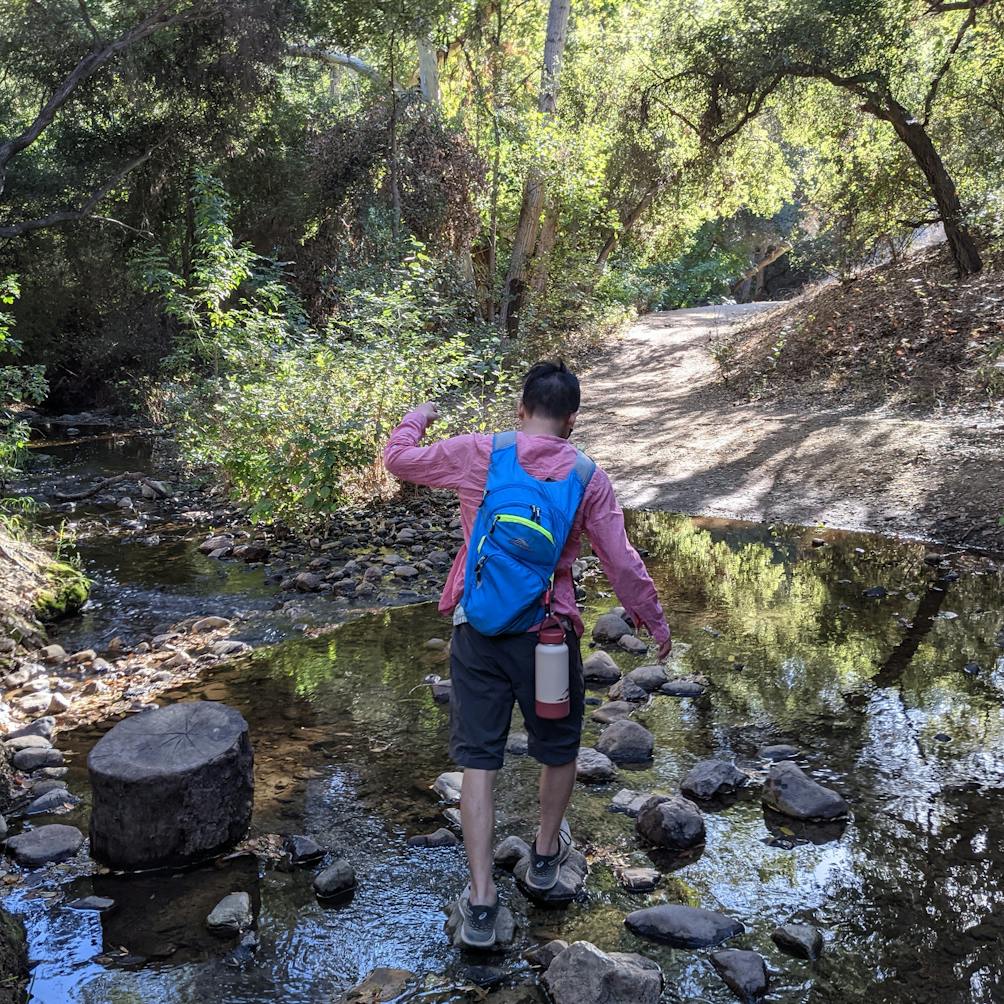 Hiker crossing Walnut Creek via some rocks at The Antonovich Trail in San Dimas 