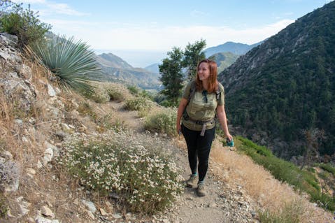 Woman hiking and smiling with big mountain views in the background on the Bear Canyon in Angeles National Forest