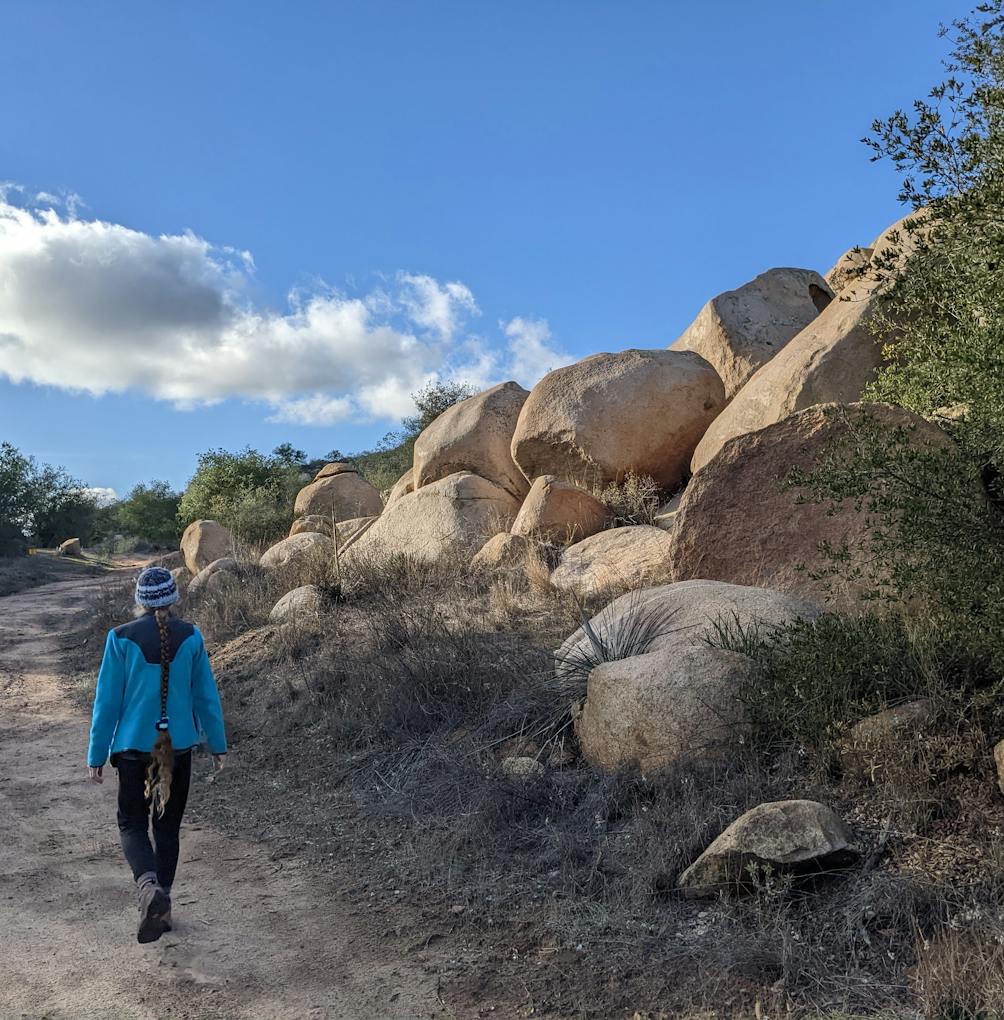 Hiker on a trail going past boulders at Daley Ranch in Escondido North San Diego County