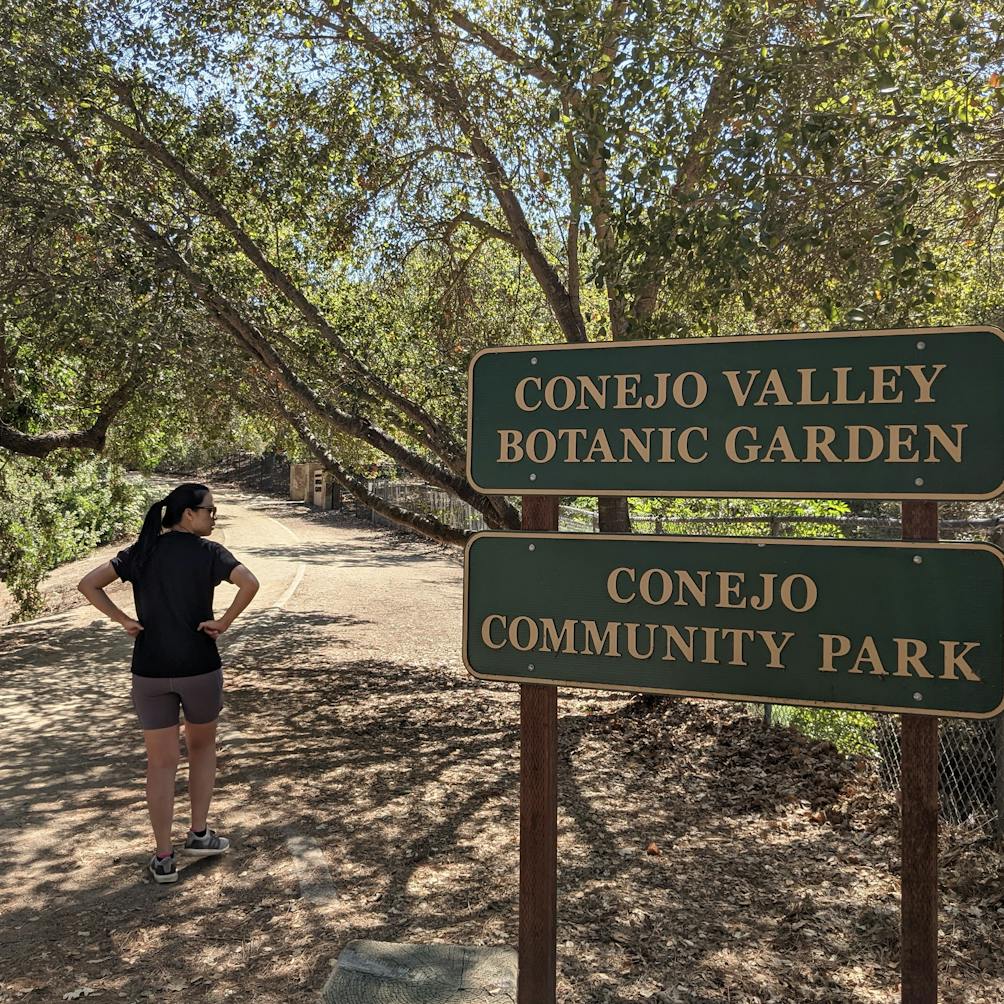 Woman passing by the official signs for Conejo Valley Botanic Garden in Conejo Community Park Thousand Oaks 