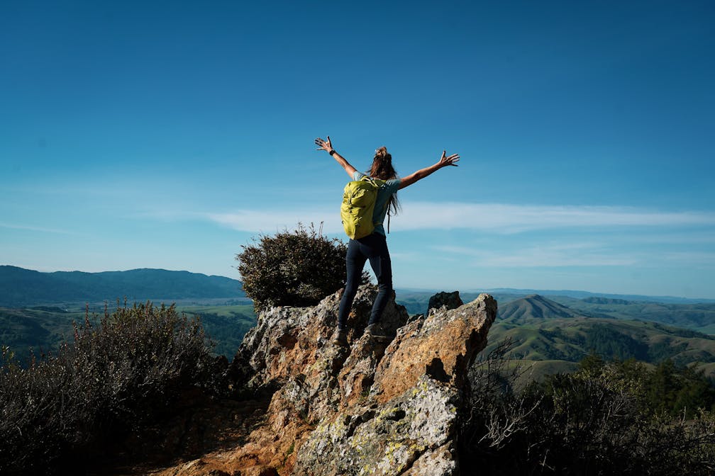 Woman with her arms outstretched to the rolling hills scenery while on a rock outcrop at Barnabe Peak in Samuel P Taylor Sate Park in Marin 
