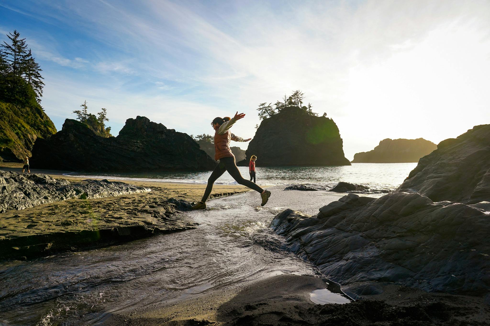 A person jumping across the estuary water at Secret Beach on the Oregon Coast 