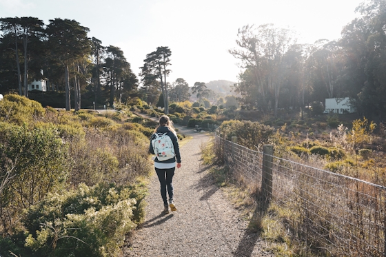 Woman wearing a white backpack walks down a winding path