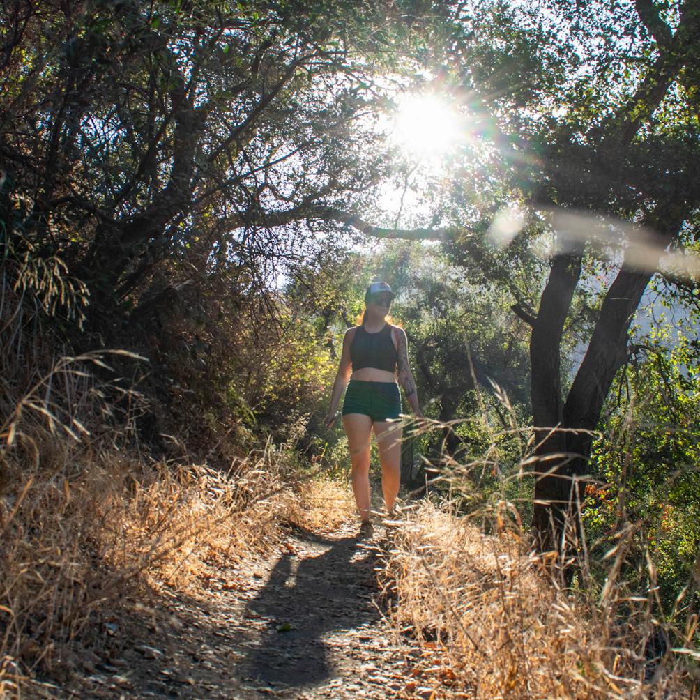 Woman hiking a forested section and sun beaming through on the Keiser Trail at Big Dalton Canyon Wilderness Park in Los Angeles County 