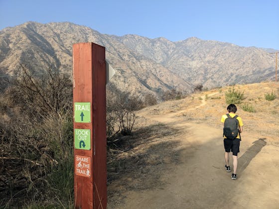 Hiker passing the trailhead post and looking towards the mountains at Hillside Wilderness Preserve in Monrovia