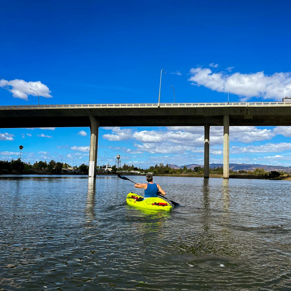 Kayaker paddling under a bridge on the Napa Valley River with Napa Valley Paddle 