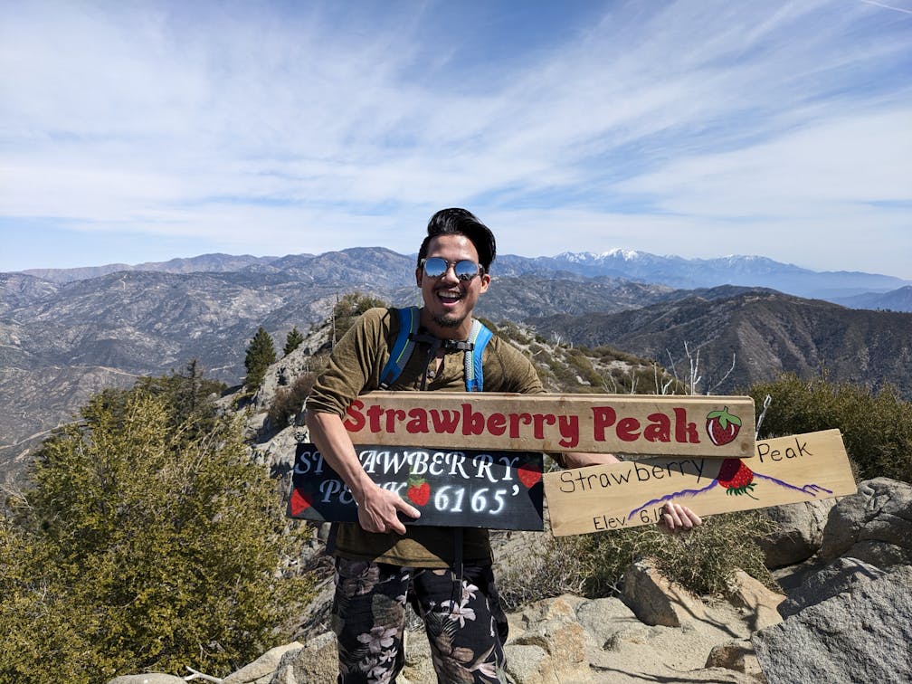Hiker holding up Strawberry Peak sign at the summit of Strawberry Peak in the San Gabriel Mountains