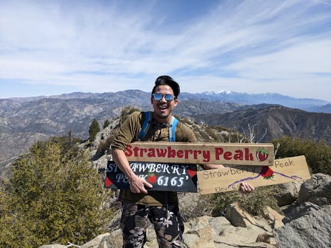 Hiker holding up Strawberry Peak sign at the summit of Strawberry Peak in the San Gabriel Mountains