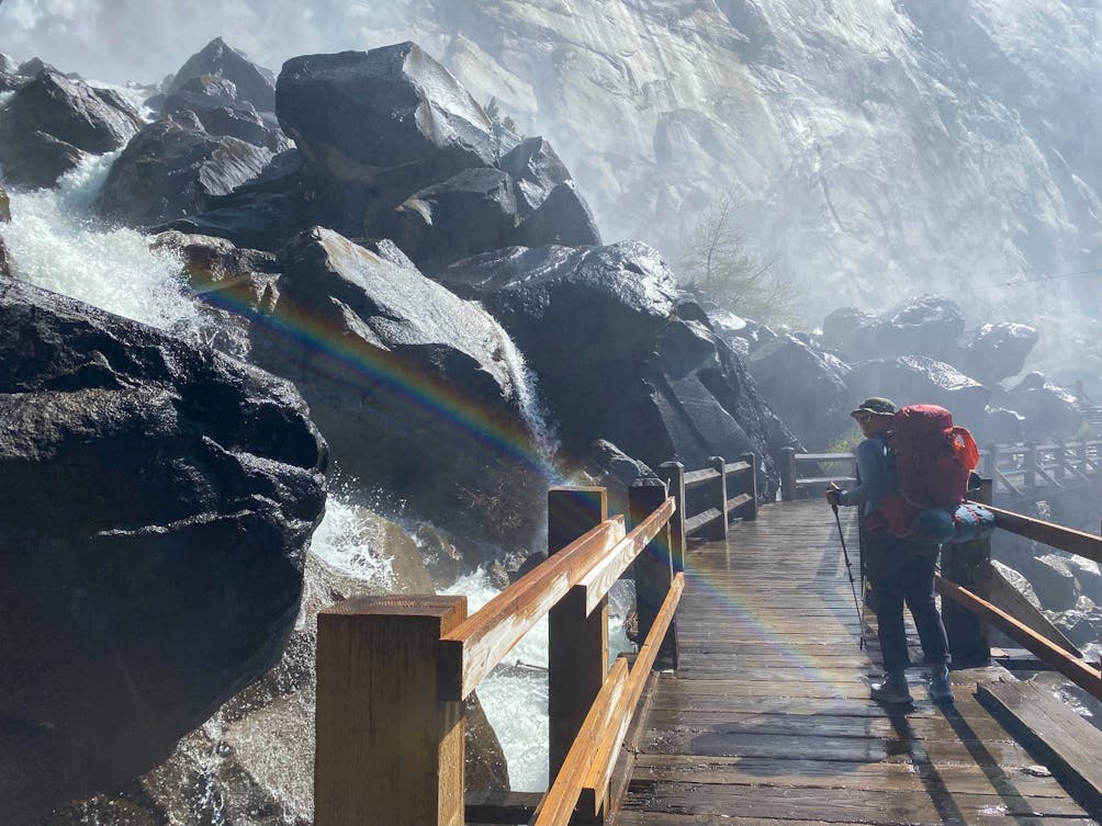 Backpacker crossing a bridge with a waterfall in Yosemite Hetch Hetchy 