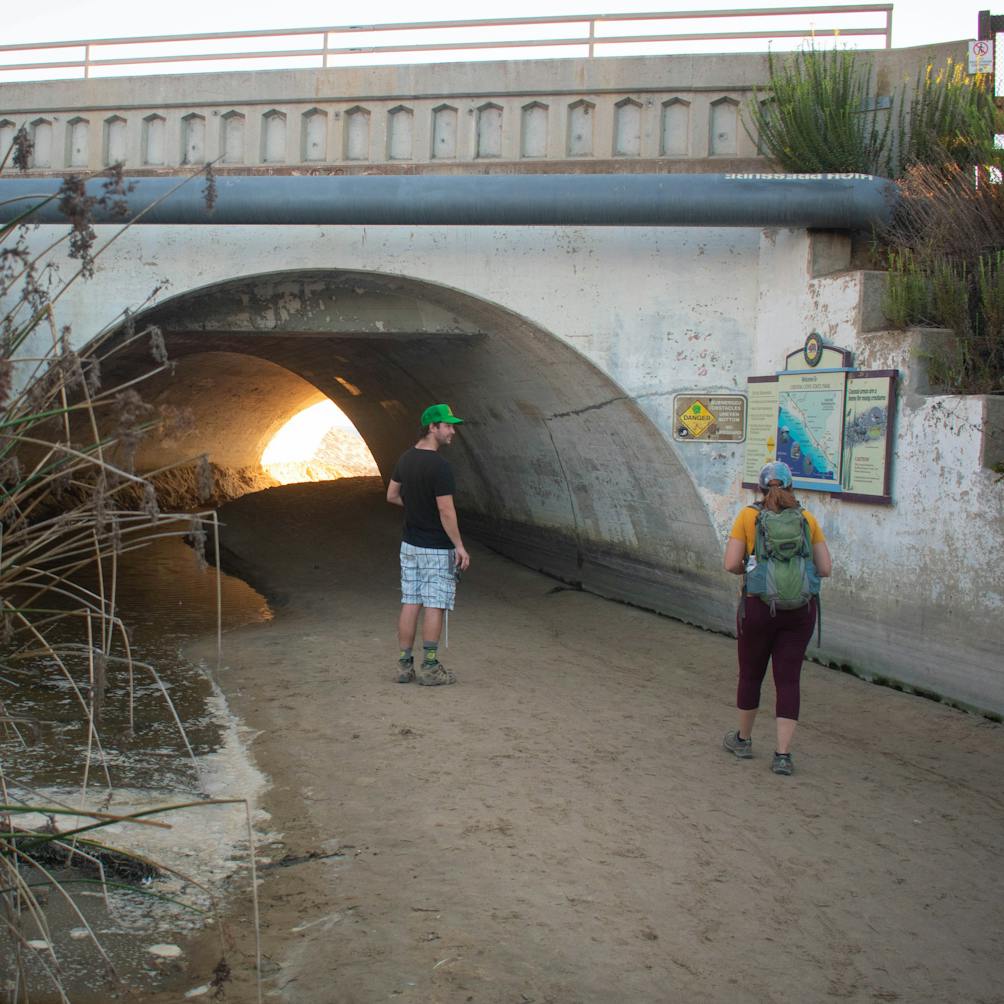 Two hikers passing through a tunnel leading to Crystal Cove State Beach in Orange County Southern California